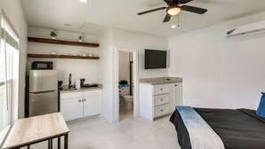 Ein kleines Zimmer mit Bett, Schreibtisch, Küchenzeile und Deckenventilator.