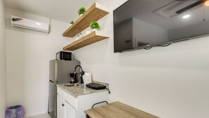 Une cuisine compacte équipée d’un réfrigérateur intégré, d’un four à micro-ondes, d’un évier et d’un plan de travail en bois. Des étagères en bois se trouvent au-dessus du plan de travail, et un téléviseur à écran plat est fixé au mur.