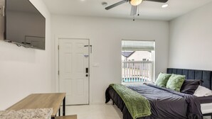 Une chambre à coucher comprenant un lit, un bureau, une chaise, une fenêtre avec des stores et un ventilateur de plafond.