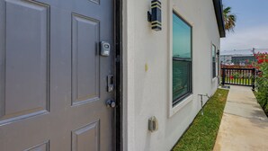A modern building with a grey door, a window, and a small garden area. - Beach Base for Groups! SPI Studio w/ Pool On-Site (South Padre Island)