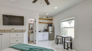 A bedroom with a bed, a TV, a ceiling fan, and a view of the kitchen. - Beach Base for Groups! SPI Studio w/ Pool On-Site (South Padre Island)