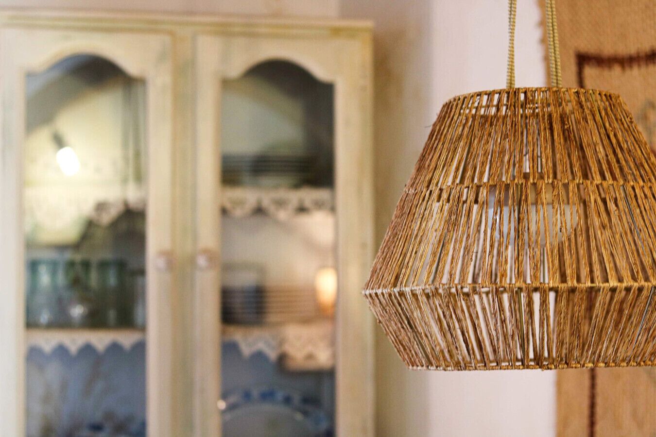 A wicker pendant light fixture in a room with a cabinet in the background.