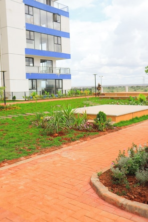 Edifici modern amb teulada plana i un balcó, envoltat d'un jardí paisatjistic amb diverses plantes i un camí pavimentat.