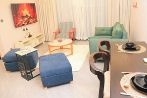 Un salon comprenant un canapé, un pouf, une table basse et une table à manger préparée pour deux personnes.