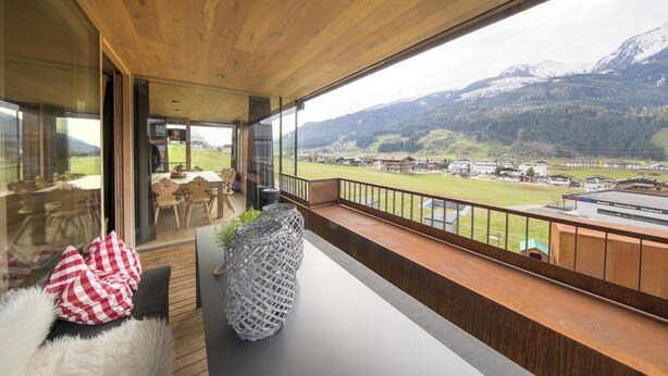 A balcony with a view of a mountainous landscape, a dining area with chairs and a table, and a large decorative vase. - Alpine Stay, Sauna & Fireplace (Bramberg am Wildkogel)