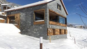 A modern chalet with a stone facade, large windows, and a wooden balcony. - Alpine Stay, Sauna & Fireplace (Bramberg am Wildkogel)