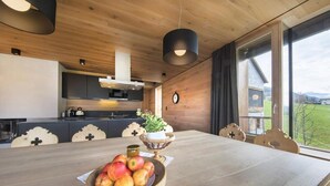 Un intérieur en bois avec une table à manger, un panier de fruits et une vue sur l’extérieur.