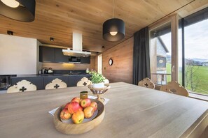 A wooden interior with a dining table, a bowl of fruit, and a view of the outdoors. - Alpine Stay, Sauna & Fireplace (Bramberg am Wildkogel)