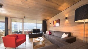 A modern living room with a sofa, red armchair, and a flat-screen TV. - Alpine Stay, Sauna & Fireplace (Bramberg am Wildkogel)