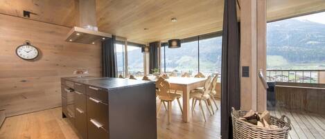 A modern kitchen with wooden cabinetry, a central island, and a dining area with a view of the mountains.