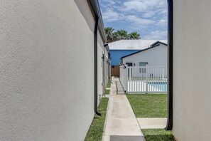 A narrow pathway leading to a pool area with a white fence and a building with a blue roof. - SPI Stay in Entertainment District, Pets Welcome! (South Padre Island)