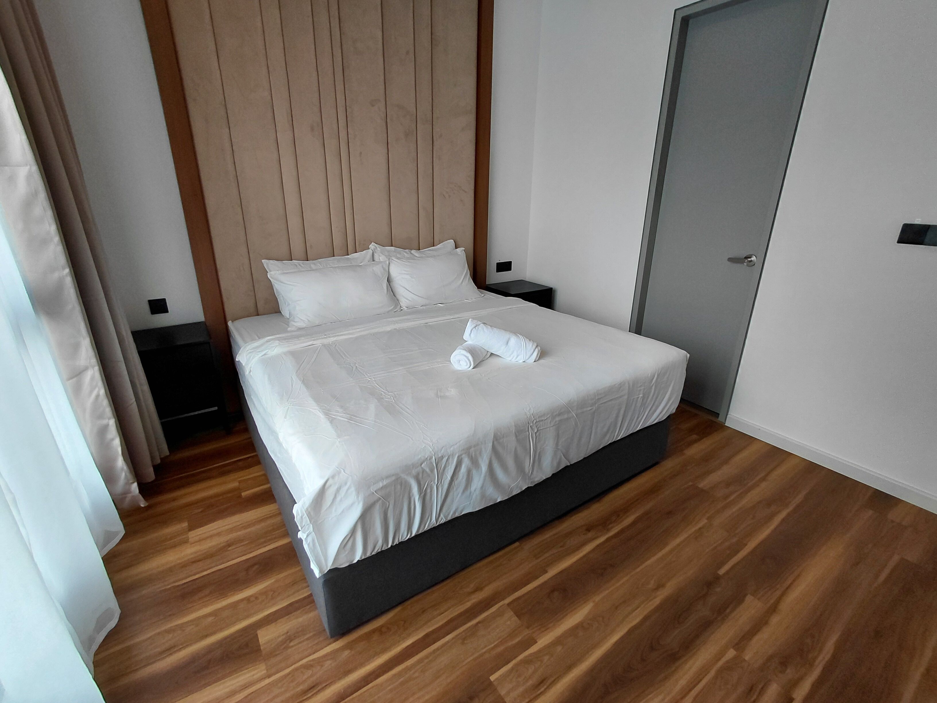 A neatly made bed with white linens, a wooden headboard, a bedside table, and a door to the right.
