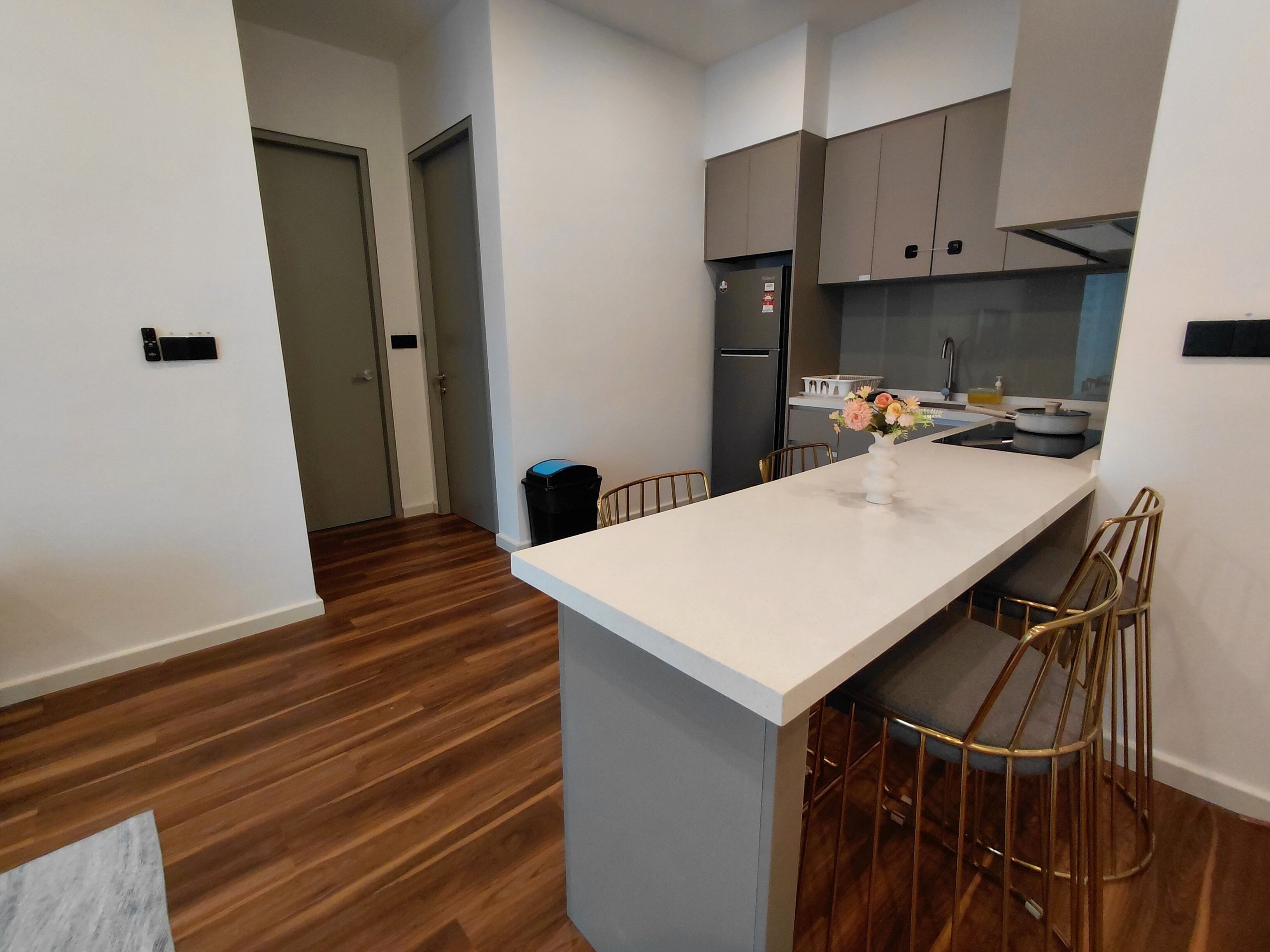 A modern kitchen with a central island, wooden flooring, and a view into the adjacent living area.