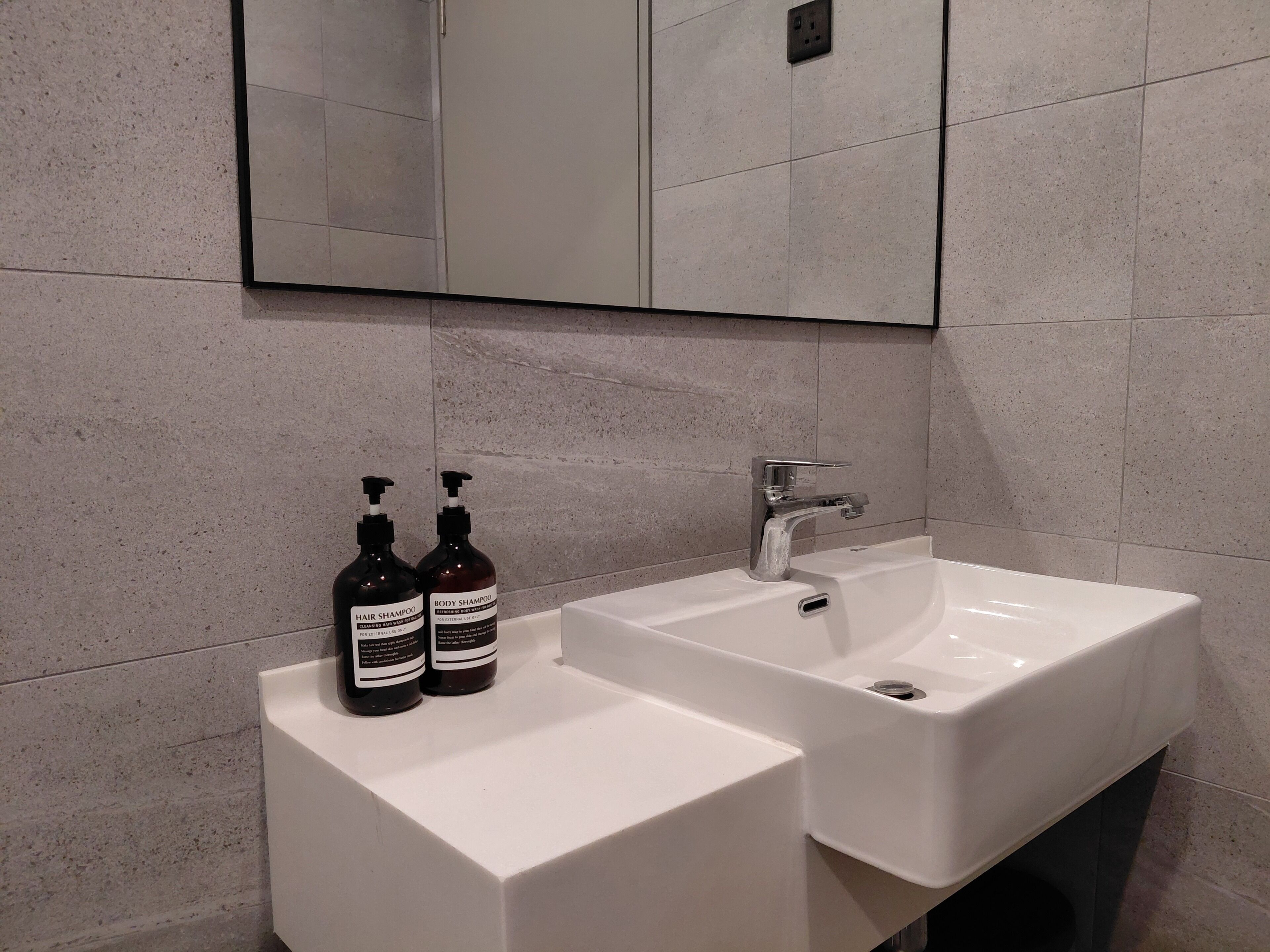 A bathroom with two sinks, a mirror, and two bottles of shampoo.