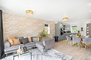 A modern living room with a sectional sofa, a glass coffee table, and a marble-patterned wall.