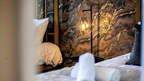 Ein Schlafzimmer mit einem Bett, Kissen, einem Nachttisch, einer Lampe und einer Marmorwand.