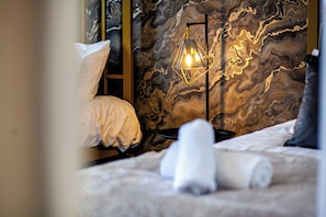 A bedroom with a bed, pillows, a nightstand, a lamp, and a marble wall.