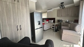 A modern interior with a kitchenette, a bed with red pillows, and a dining area. - Arise Boutique Guesthouse (KuGompo City)