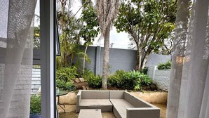 A patio with a sectional sofa and ottoman, surrounded by plants and a concrete floor. - Arise Boutique Guesthouse (KuGompo City)