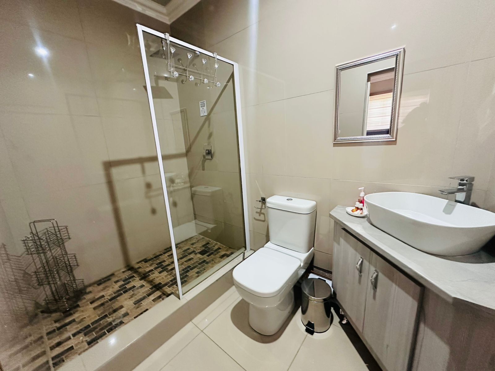 A bathroom with a glass shower enclosure, a toilet, a sink, and a trash bin.