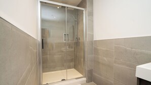 A modern bathroom with a glass-enclosed shower, a white sink, and a beige tiled floor. - Church House by Guestz (Filton)