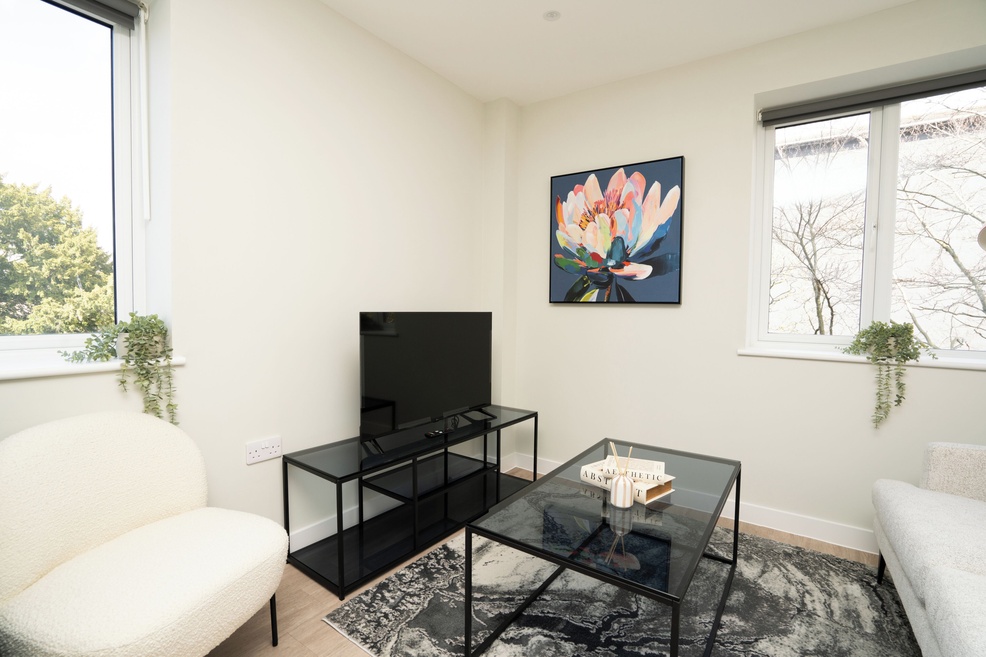 Un salon moderne avec un téléviseur à écran plat, une table basse en verre, un canapé blanc et un tableau accroché au mur.