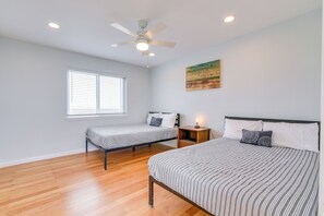 Un dormitorio con dos camas individuales, un ventilador de techo, una ventana con persianas y un cuadro en la pared.