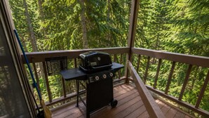 A wooden deck with a grill, a broom, and a chair. - Rustic Charm Condo #16 at Ptarmigan Village (Whitefish)