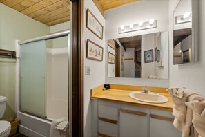 A bathroom with a glass shower enclosure, a sink with a wooden countertop, and a mirror with lights. - Rustic Charm Condo #16 at Ptarmigan Village (Whitefish)