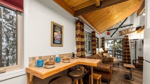 A cozy interior with a wooden bar, seating area, and large windows. - Rustic Charm Condo #16 at Ptarmigan Village (Whitefish)