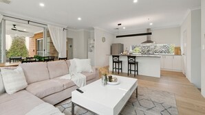 A modern living room with a sofa, coffee table, and a kitchen area with bar stools. - 3BR Comfortable Home (Edgewater)