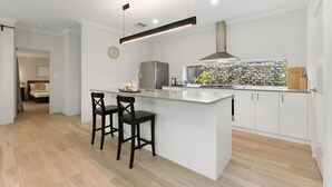 A modern kitchen with a central island, bar stools, a stainless steel refrigerator, and a large window with a view of foliage. - 3BR Comfortable Home (Edgewater)