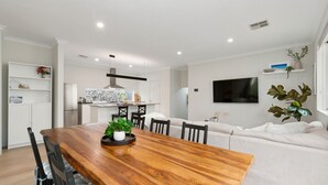 A modern kitchen with a central island, a dining area with a wooden table, and a living area with a sofa and TV. - 3BR Comfortable Home (Edgewater)