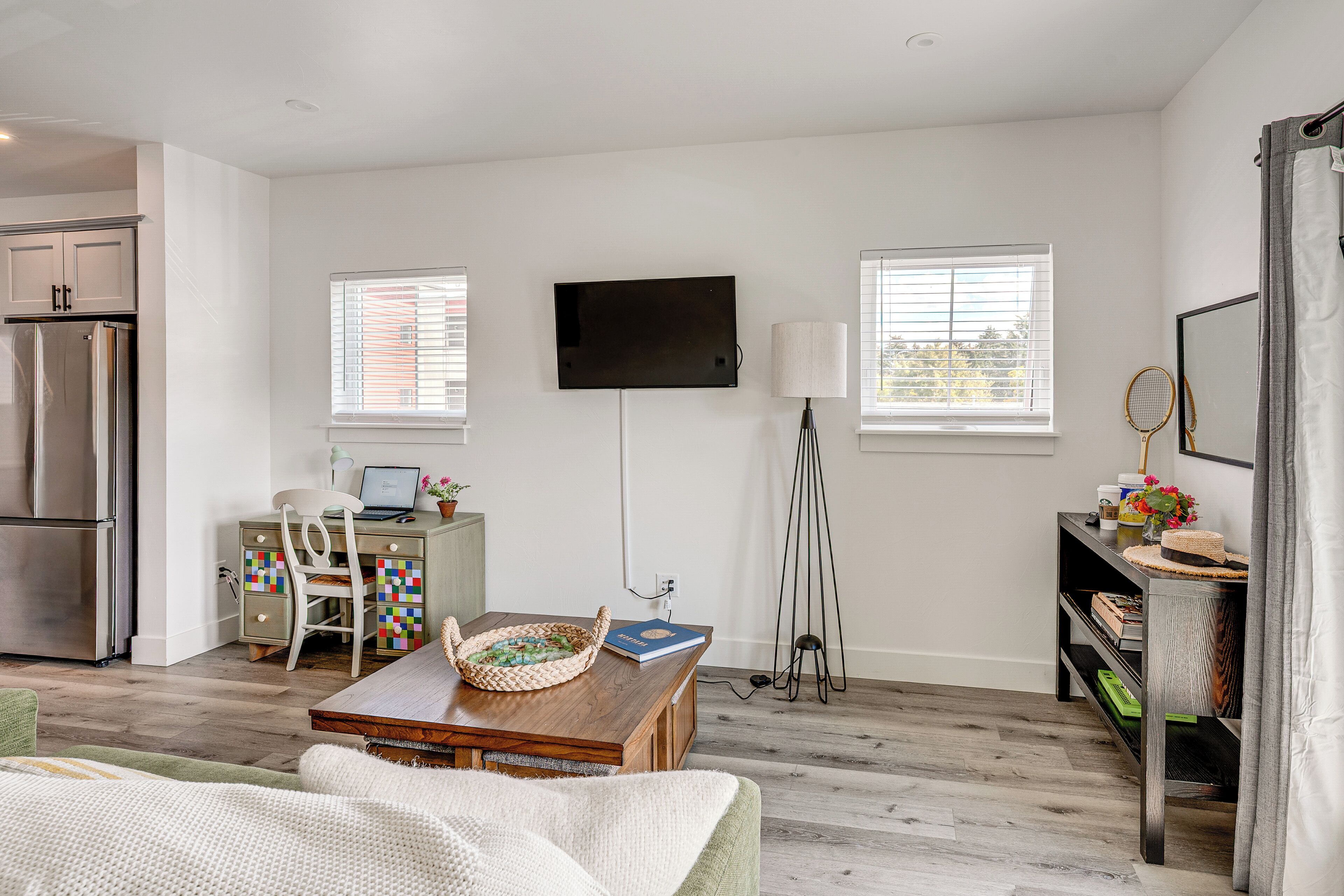 A modern living room with a flat-screen TV, a dining table, a sofa, and a kitchen area with a refrigerator.
