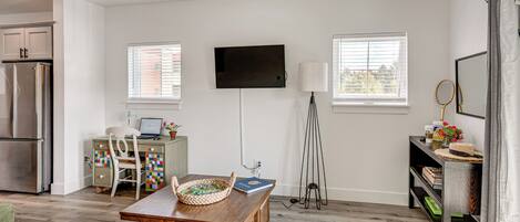 A modern living room with a flat-screen TV, a dining table, a sofa, and a kitchen area with a refrigerator.