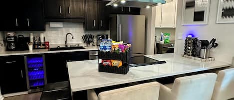 Una cocina moderna con una isla central, armarios negros, electrodomésticos de acero inoxidable y un enfriador de vinos empotrado.