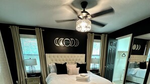 Camera da letto con un letto grande, una ventola a soffitto, un comodino, uno specchio e vista esterna.