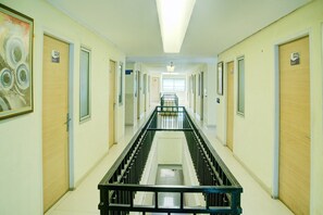 A long, narrow hallway with doors numbered 024 to 025, a central staircase, and a ceiling light.