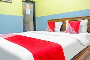 A bed with a white and red bedspread, a wooden headboard, and two patterned pillows.