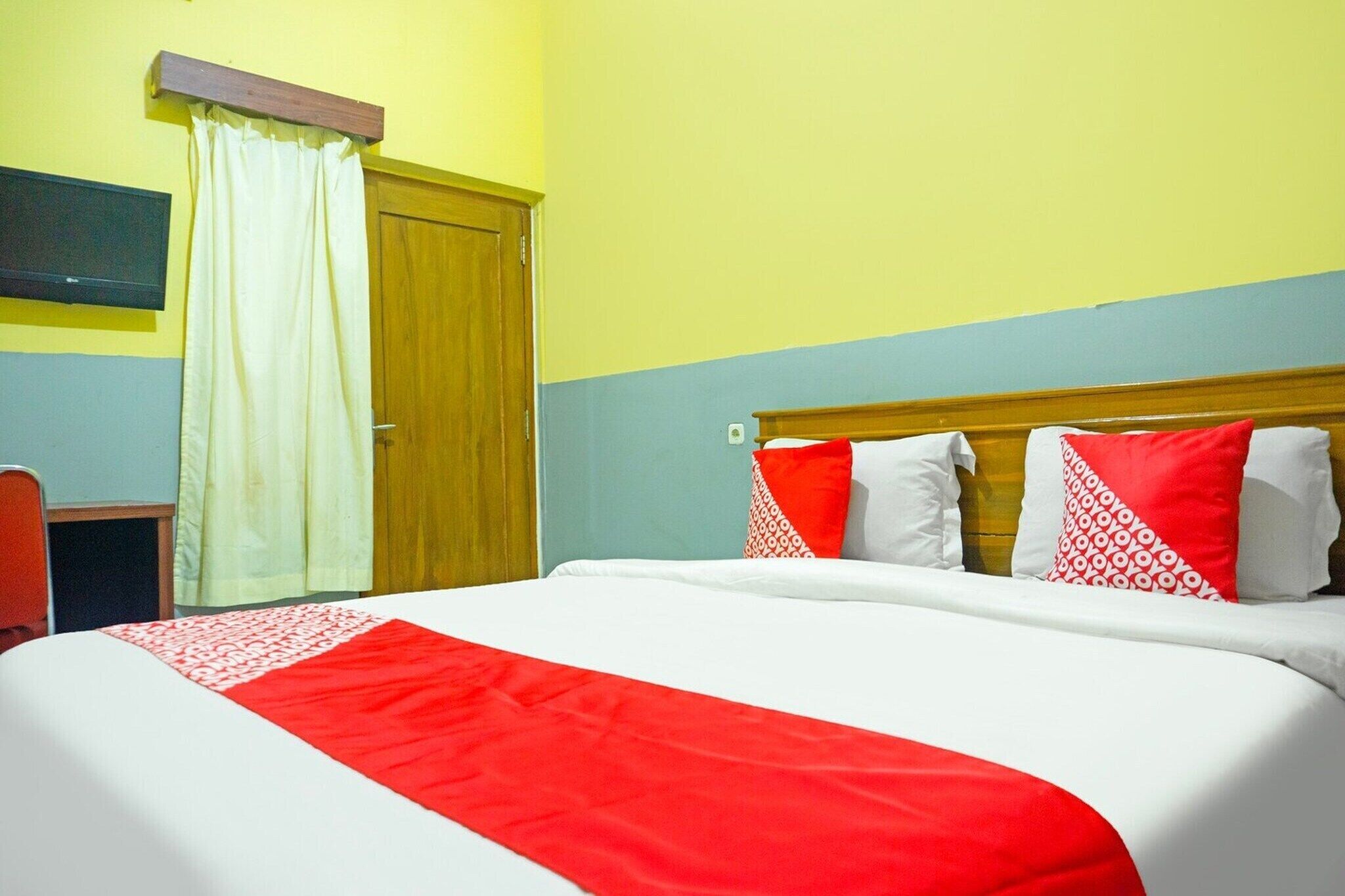 Une chambre d’hôtel avec un lit, un bureau et un téléviseur fixé au mur.