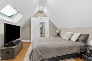 A bedroom with a TV, a bed, a lamp, and a suitcase. - Charming Roncesvalles Home · High Park · BMO Field (Toronto)