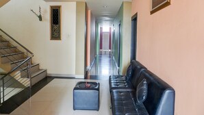 Eine Hotelhalle mit einer Treppe, einem schwarzen Ledersofa, einem kleinen Hocker und einem Flur, der zu einer Tür führt.