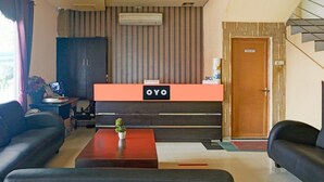 Ein Empfangsbereich mit einer Rezeption mit dem Schild 'OYO', einer Holztür mit der Beschriftung 'TOILET' und einer Treppe rechts.