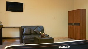 Ein Zimmer mit einer schwarzen Ledersofa, einem kleinen Holzschrank und einem an der Wand befestigten Fernseher.