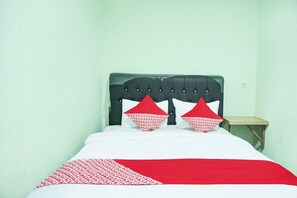 Un letto con testiera nera, biancheria rossa e bianca e un comodino in legno.