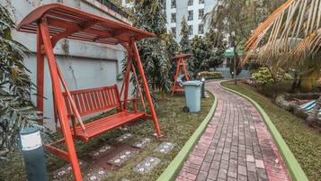 A pathway leading to a red bench with a metal frame, surrounded by greenery and a brick path.
