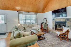 A living room with a wooden ceiling, a stone fireplace, a sofa, a coffee table, and a television. - Game Room! Family Escape on Tims Ford Lake (Winchester)