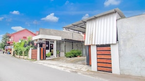 A residential building with a garage, a covered entrance, and a red building in the background. - Cozy Double Escape W/ Free WiFi and Parking (Yogyakarta)