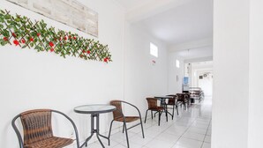 A corridor with wicker chairs and tables, white walls, and a decorative plant. - Cozy Double Escape W/ Free WiFi and Parking (Yogyakarta)
