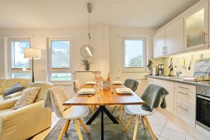 Une cuisine moderne avec des meubles blancs, une table à manger pour quatre personnes et un canapé dans l’espace salon.